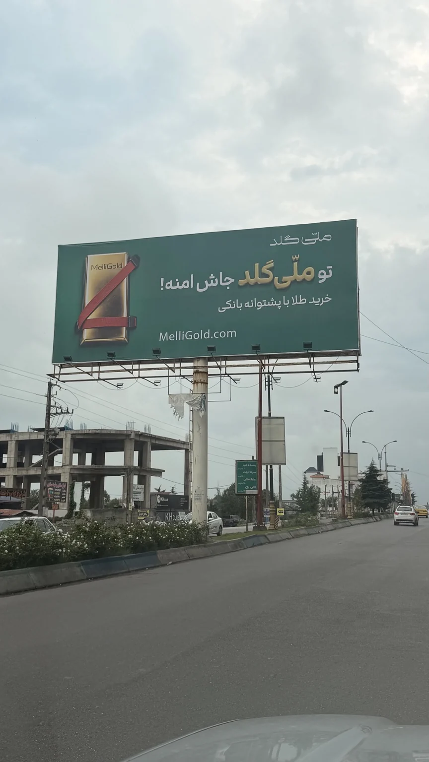 بیلبورد ملیگلد با شمش طلای بستهشده با کمربند ایمنی قرمز و شعار تو ملیگلد جاش امنه